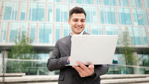 Man looks at laptop outside modern office building