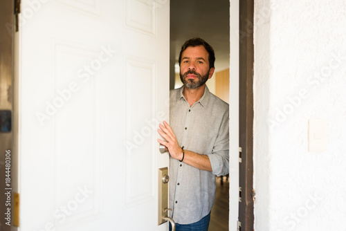 фотографія Latin man opening front door, cautiously looking out, welcoming visitors or home