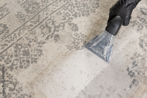 Fotografija Vacuum nozzle washing vintage rug with bright cleaned path