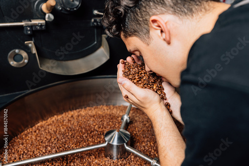 Photos Close up of young barista smelling fresh roasted coffee beans at drum of the mac