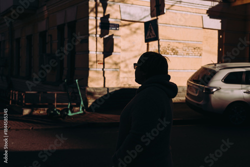 Canvas Print A person in silhouette on an urban street, bathed in harsh, contrasting sunlight that creates dramatic shadows against a city buildings