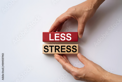 Minimalist flat lay of 'LESS STRESS' wooden blocks, symbolizing wellness and mindfulness, supported by hands on a clean white background, perfect for business or self-care themes.