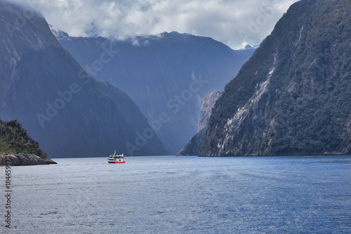 Fotografie Misty cruise boat cruising through Milford Sound surrounded by dramatic fiord la