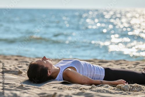 Fototapeta Naklejka Na Ścianę i Meble -  Young woman practicing mindfulness yoga lying on sandy beach by Baltic Sea