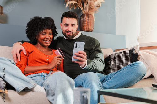 A couple shares a delightful moment while shopping online, using a smartphone and credit card on their cozy couch, showcasing the joy of digital shopping together in the comfort of home.