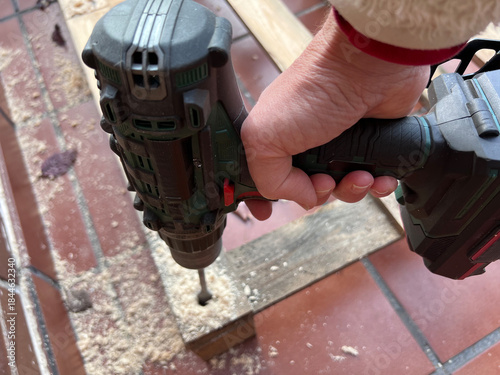 Proceso de perforación de palets de madera con broca pala para crear una base estructural. Imagen mostrando trabajo visto desde lateral superior. Mano sujeta taladro.