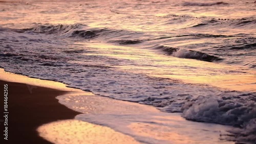 At sunset, waves crashing onto the shore on the beach.