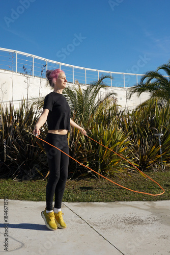 A woman skipping rope outdoors on a sunny winter day, practicing simple everyday fitness, healthy lifestyle. Casual Sportswear, jumping rope. Tropics winter