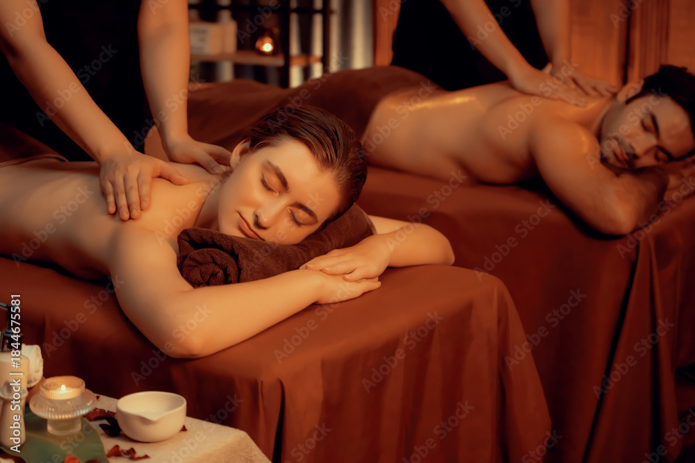 Obraz premium Caucasian couple customer enjoying relaxing anti-stress spa massage and pampering with beauty skin recreation leisure in warm candle lighting ambient salon spa at luxury resort or hotel. Quiescent