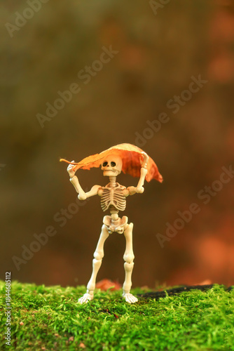 Toy skeleton figurine holding dry leaf over head in fairy tale autumn forest