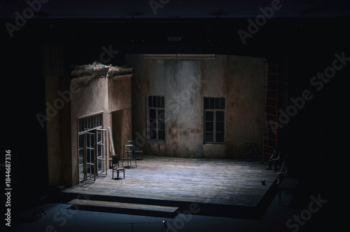 Empty theater stage with a realistic dramatic set, aged walls and wooden floor, prepared for rehearsal or performance, moody lighting creating a cinematic atmosphere.