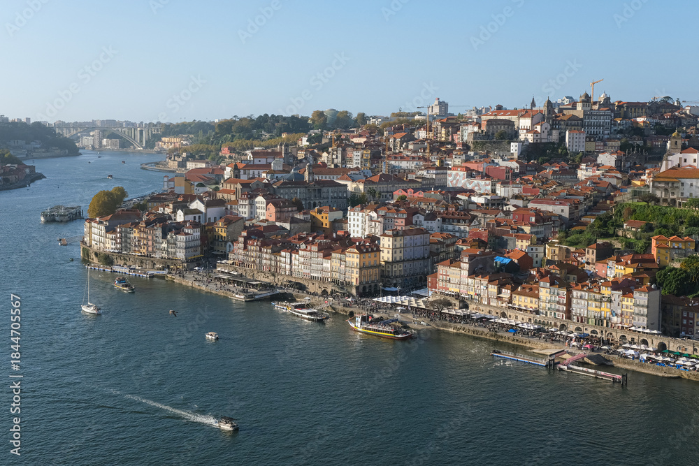 Fototapeta premium Scenic panoramic view of Porto, Portugal, with colorful historic buildings along the Douro River, traditional boats, and clear blue sky on a sunny day