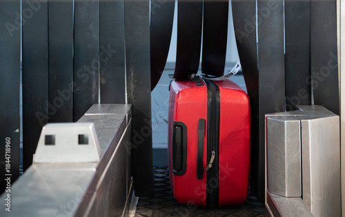 Red suitcase moving through an automated baggage screening machine at an airport security checkpoint during luggage processing