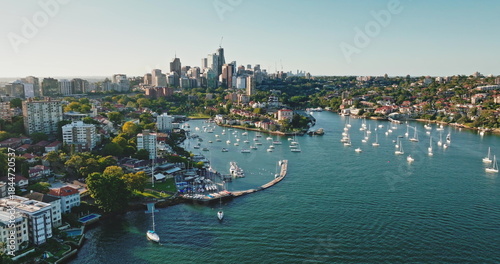 Bild auf Leinwand Sydney harbor cityscape with many sailboats and yachts moored in tranquil bay, residential buildings skyscrapers, green trees lining shore, central business district skyline in distance