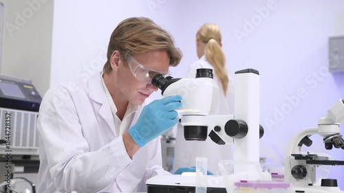 Scientist examines samples using a microscope in a modern lab with another researcher