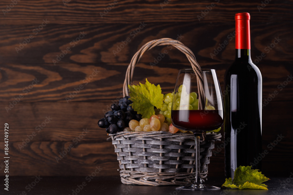 Obraz premium Red wine bottle with a glass and basket of fresh grapes