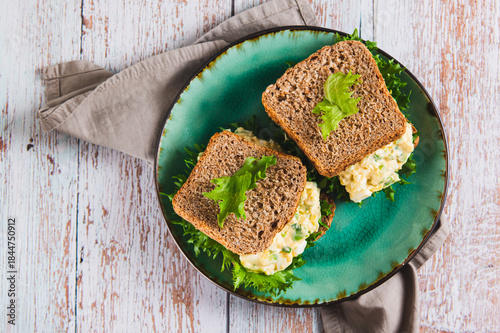 Fotografie Close up of savory egg salad sandwich with avocado on whole grain bread on a pla