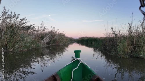 Boat sailing on albufera lake at twilight, calm water reflecting reeds and trees