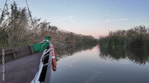 Boat sailing on albufera lake at twilight, calm water reflecting reeds and trees