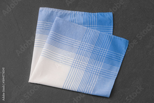 A folded blue and white patterned cotton handkerchief on a dark gray background.