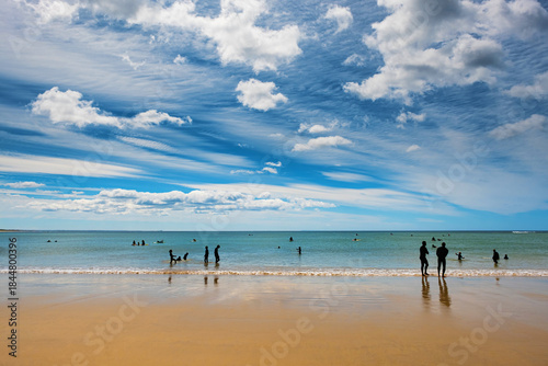 Silhouetted beachgoers enjoy calm water beneath vivid, wispy cloud patterns