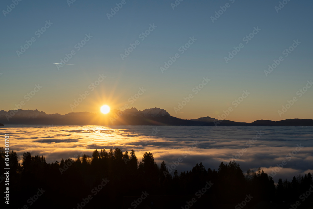 Obraz premium sunset over the summits of high mounatins above a sea of fog towards clear blue and orange sky in late autumn