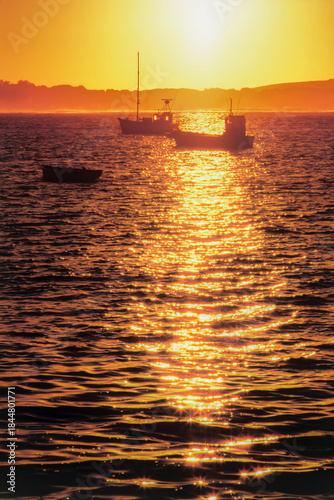 A peaceful ocean sunset with silhouetted boats and shimmering reflections of golden light on the water
