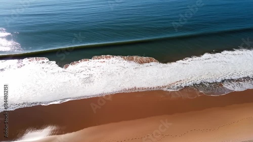 A tranquil scene featuring gentle ocean waves lapping against a pristine sandy beach under a clear blue sky. ideal for designs emphasizing relaxation, nature, and coastal vacation themes.