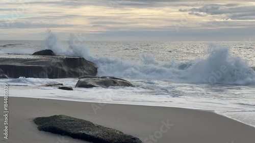 Ocean waves crashing against rocky coastline under gray sky