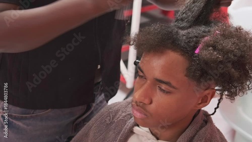 Teen boy at start of braiding process with afro hair sectioned, stylist marking and combing a strand with fine-tooth comb