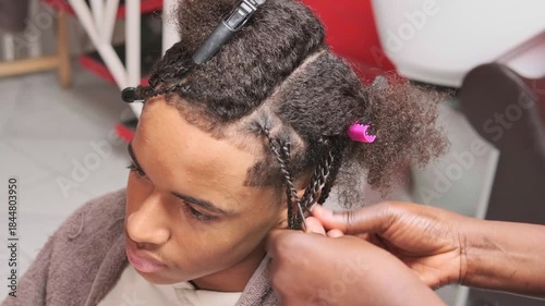 Afro stylist’s hands braiding a teenager’s hair in a barbershop, detailed top-view shot