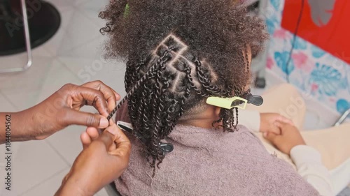 Back view of teen boy’s head with neatly sectioned afro braids as stylist continues braiding a strand on top