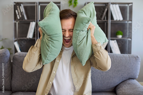 Foto Angry stressed man with pillows blocks noise from neighbors on sofa at home