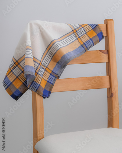 A folded white handkerchief with a yellow, blue, and black plaid border is draped over the wooden backrest of a chair.