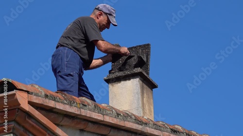 A chimney sweep removes dirt from the inside of a chimney cap on a roof