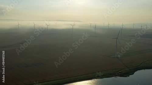 Beautiful aerial morning landscape with lake and windmills or wind turbine in fog on wind farm in rotation, 4k