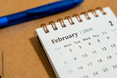 Fotografie Close-up view of a desk calendar displaying the month of February 2026 with a blue pen nearby