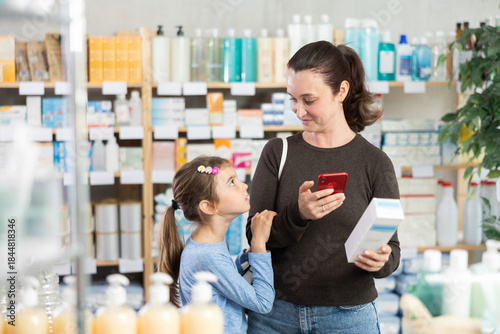 Adult woman with daughter buyers scanning qr code for moisturizing cream in pharmacy