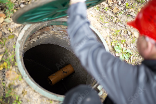 A worker leans over a septic tank, showing a sewage drain pipe.
