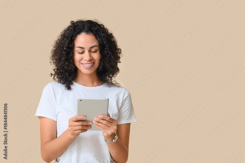 Fototapeta premium Young African-American woman working with tablet computer on beige background