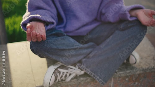 Woman sits cross-legged on a stone surface practicing meditation in a green park during evening hours with soft light
