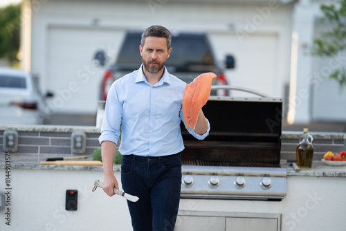 Cooking fish in backyard. Middle aged Hispanic man grill salmon barbecue. Barbecue and grill. Roasting and grilling food. Chef man do BBQ fish. Man cook herb crusted salmon in the kitchen