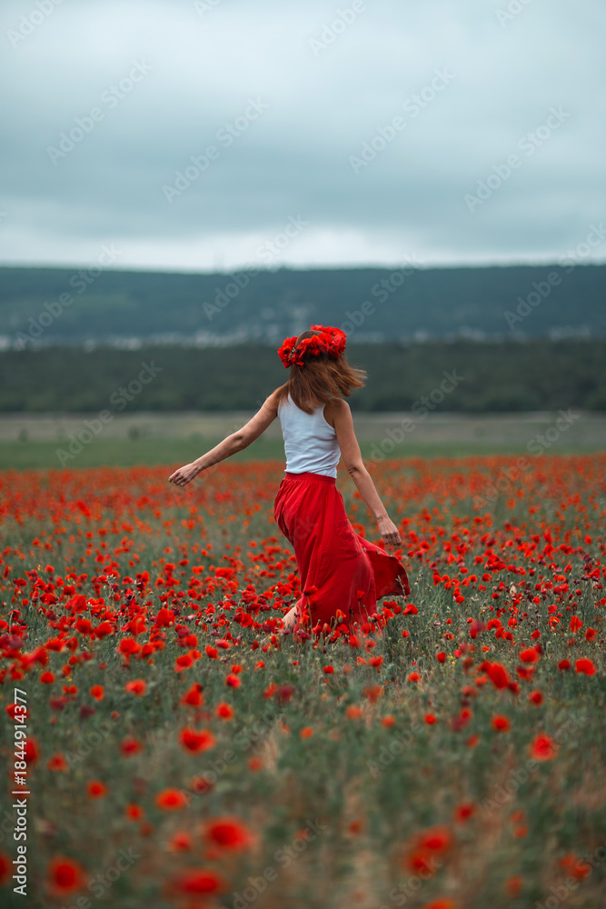 Naklejka premium Woman poppies field running freely through vast spring flowers and dramatic sky