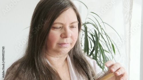 wooden comb, brush in female hand, woman combing long brown hair, tangles of fallen hair wound on brush pins, concept hair loss, health, causes, symptoms and treatment alopecia, hormonal imbalance