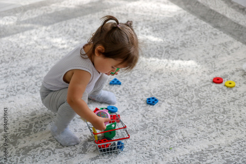 A little girl at home collecting toys in a basket