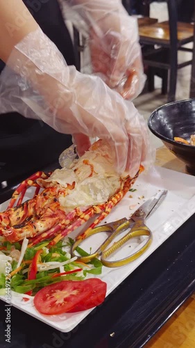 Vertical video. Hands wearing Gloves opening a Cooked Lobster on a White Plate with Vegetables in a Close Overhead angle, Seafood Preparation Concept