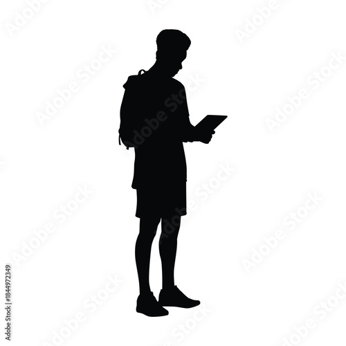 Silhouette of a Young Man or Student Standing with a Backpack, Using or Reading a Digital Tablet or E-Reader Device