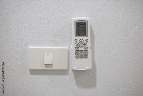 The light switch and remote control for the air conditioner are mounted on a white wall.