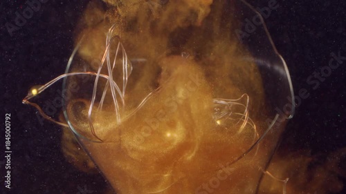 Defocused shiny splash. Old light bulb. Yellow golden powder ink fluid drop in broken night glass lamp. Fume color abstract black background.