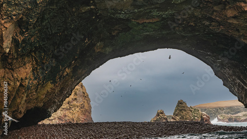 Photography Through the natural stone arch, you can see the pebbly shore of the bay, rocks against the blue sky